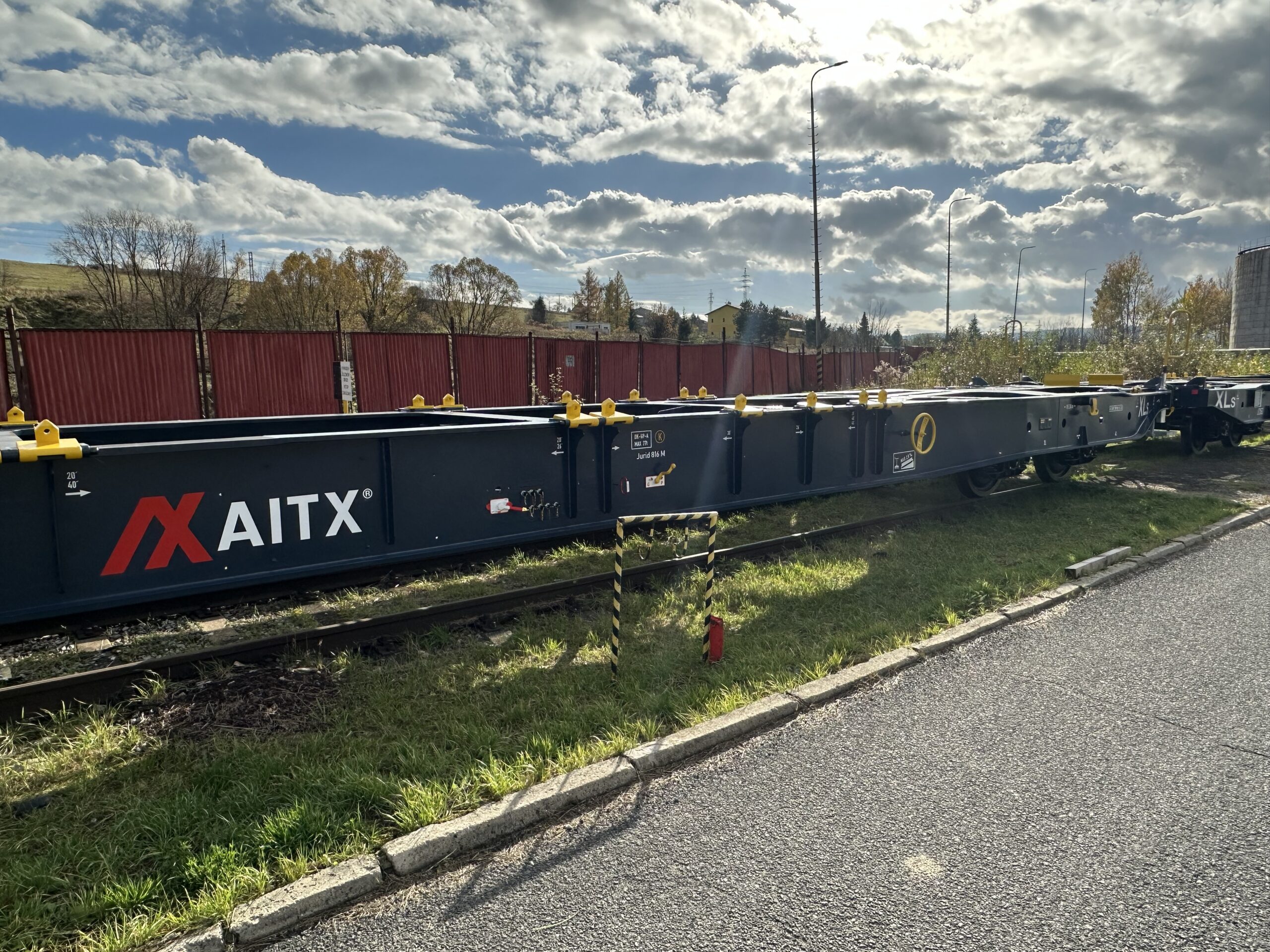AITX branded rail freight container sitting on tracks in a European industrial area, with cloudy skies and autumn foliage in the background.