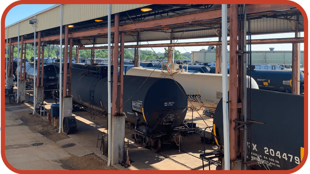 Tank cars lined up under a shelter in a railway yard, showcasing a variety of tank sizes and types, essential for planning tank qualification strategies in the transportation industry.