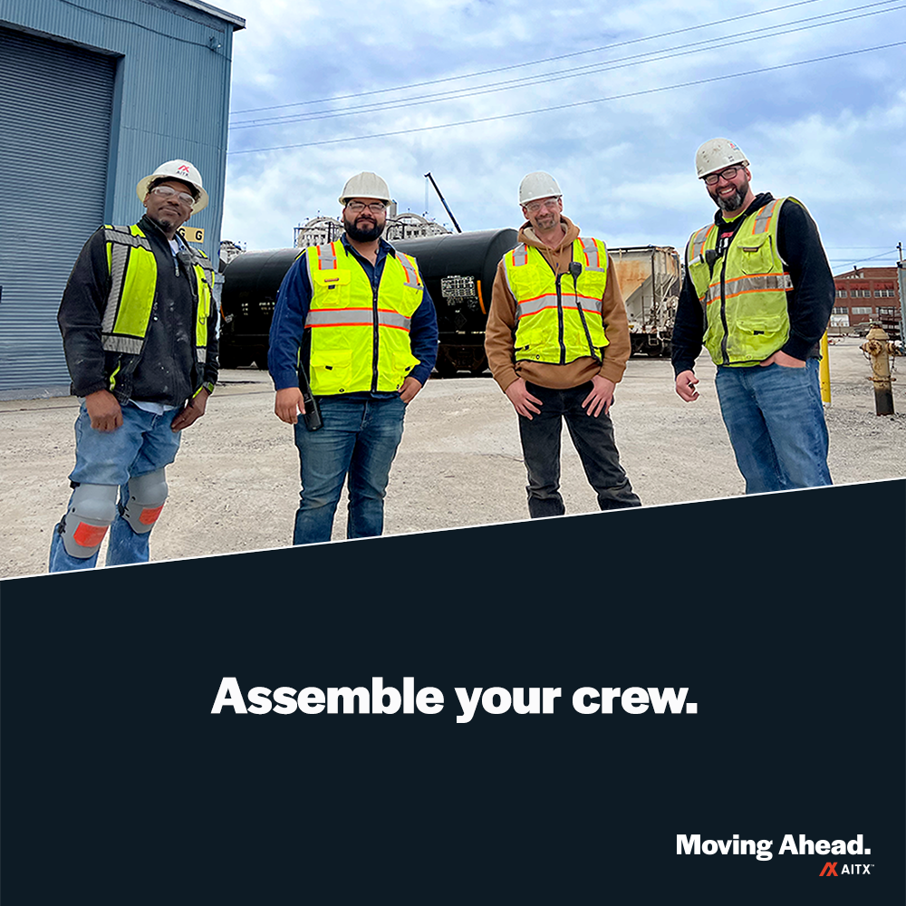 Group of four construction workers wearing safety vests and hard hats, standing confidently at a job site with industrial equipment in the background. Promotes teamwork and safety in construction.
