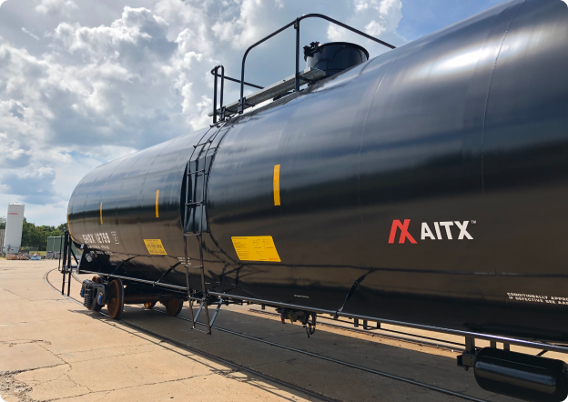 Black freight train tank car with safety markings and the AITX logo, parked on a railway track under a partly cloudy sky.