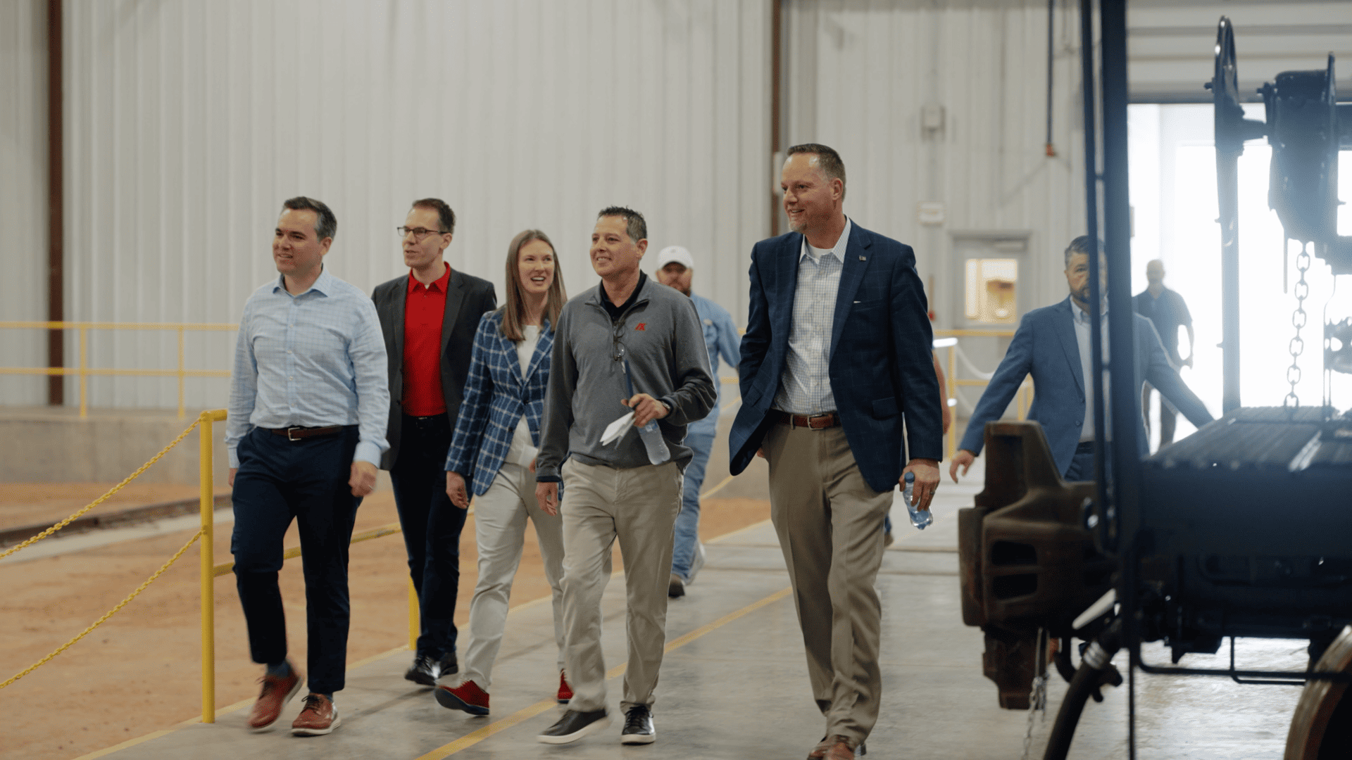 Group of professionals walking through a spacious industrial facility, engaging in conversation, showcasing teamwork and collaboration in a business environment.